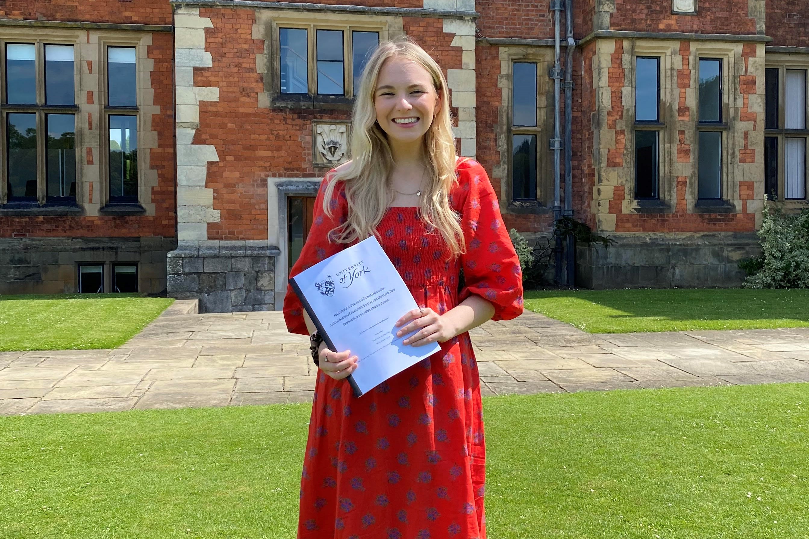Anna Clark smiling at camera holding her dissertation